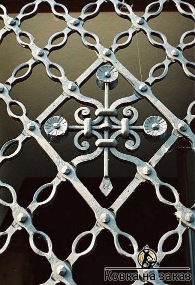 Кованая решетка на окно с фигурной центральной розеткой и металлической сеткой внахлест из кованой полосы на клёпках