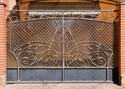 Кованые ворота и калитка выполнены в едином стиле - нижняя часть закрыта «наглухо» листовым металлом с декоративными клёпками